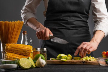 A professional chef cuts zucchini to make a salad with seafood, shrimp. On a gray background with ingredients.