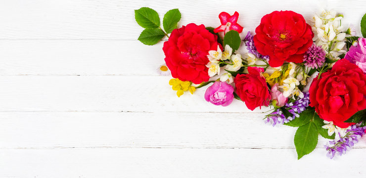 flower arrangement border of different wildflowers and garden flowers of red roses, peonies and jasmine flowers on a white wooden background with copy space, top view