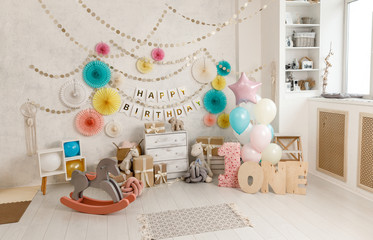 Birthday decorations with balloons, gifts, toys, garlands and candy for yearling, little baby party, selebration on a white wall background. Decor elements in unicorn colors.