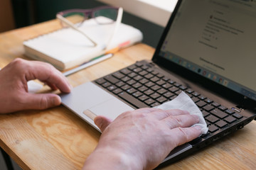 A man wipes a laptop with a wet alcohol wipe to prevent infection with coronovirus flu.