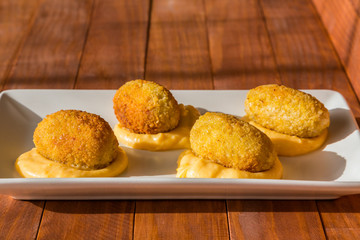 Traditional spanish snack- croquettes fried in oil, with yellow cream sauce on white plate at sunny...