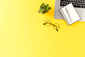 Modern office desktop with laptop, notebook, eyeglasses and pen on yellow background. Business background