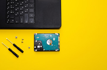 hard drive, laptop and screwdrivers on a yellow background