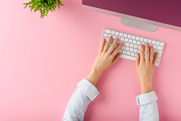 Female hands using modern computer on pink background. Office desktop. Top view