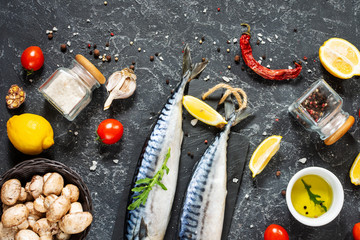 Fresh raw mackerel with lemon and spices on a black stone background.