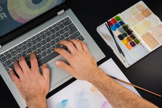 Hands of young man working on the laptop. Concept of graphic designer creating on a dark wood table.