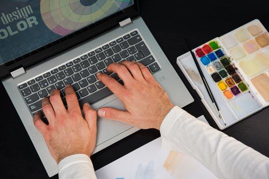 Hands of young man working on the laptop. Concept of graphic designer creating on a dark wood table.