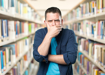 Young man wearing a blue outfit. Looking seriuos and covering his mouth with his hand.