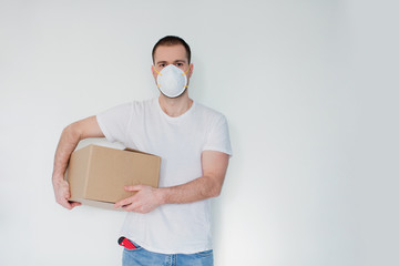 Caucasian man wearing respirator with cardboard box on a white background. Delivery man