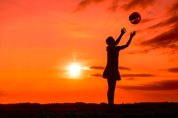 Fototapeta na wymiar Silhouette of playing girl with ball in the nature in cloudy sky background in sunset