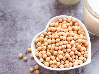 Close up soybeans in a heart-shaped bowl with soymilk in glass on grey concrete background. Plant protein. Copy space for text.