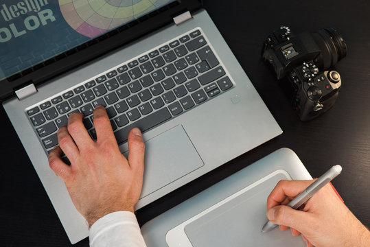 Designer creating with the laptop and graphic tablet on a wood table. Workplace of graphic designer with laptop, camera and pen tablet.