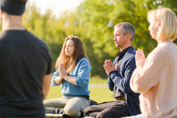 A group of young people meditate outdoors in a park. 