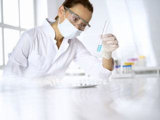 Female laboratory assistant in mask analyzing test tube with blue liquid. Medicine, health care and virus pandemic protection