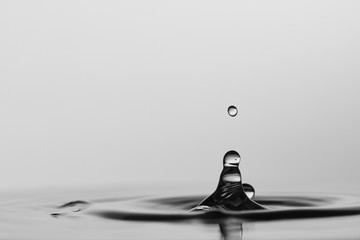 Gotas de agua cristalina chapoteando en una superfície de agua calmada y formando ondas circulares...