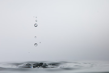 Gotas de agua cristalina chapoteando en una superfície de agua calmada y formando ondas circulares