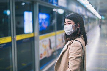 Young asian woman wearing protective face mask stand in line during waiting underground train in subway due to Coronavirus or COVID-19 outbreak situation in all of landmass in the world