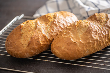 Two loafs of hot baked bread on an oven grid with a towel in the background