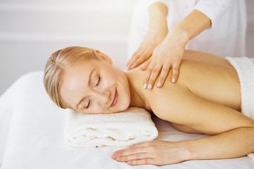 Obraz na płótnie Canvas Beautiful caucasian woman enjoying back massage sunny spa salon. Beauty concept