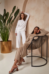 Two beautiful sexy brunette woman friends face cosmetic makeup tanned skin wear fashion clothes style beige white knitted suit sandals accessory interior furniture armchair journey summer palm boho.