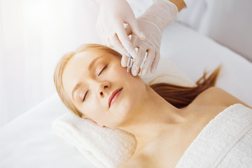 Obraz na płótnie Canvas Beautician doctor doing beauty procedure with syringe to caucasian female face in synny room. Cosmetic medicine and surgery, beauty injections concept