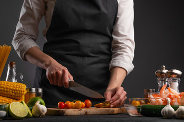 The chef cuts cherry tomatoes to make a fresh salad with shrimp, seafood. Cookery and recipe book. Restaurant cuisine. Recipes