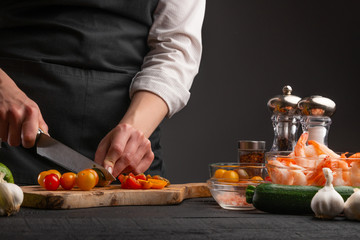 Cooking StirFry vegetables with shrimp. Chef slices cherry tomatoes, on a gray background with shrimp. Seafood