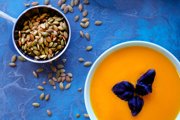 Pumpkin soup with purple Basil on a blue background with crispy toasted pumpkin seeds.