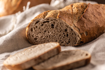 Two slices of freshly baked bread placed on top of the loaf and a linen cloth with a knife on a side
