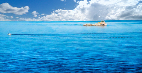 Scoglietto di Portoferraio con una barca su di un mare calmo e scie di onde.