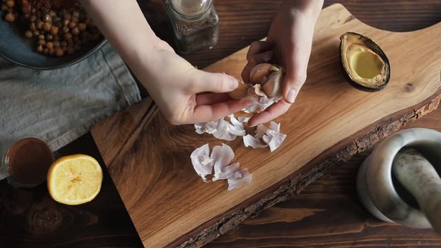 Closeup of the hands of a young woman who peel garlic on a cutting board on the kitchen table. View from above