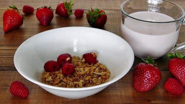 Adding raspberries inside a bowl with granola and pouring milk over
