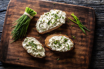 Slices of bread with a cottage cheese spread, freshly cut chives, and a bunch of chive aside placed...