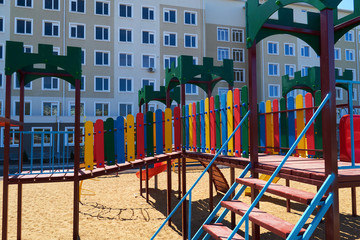 Fototapeta na wymiar Urban residential infrastructure without people - children's playground next to a condominium. Swing, slide, stairs, multistory building. A place for children to play.