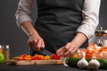 Cooking StirFry vegetables with shrimp. Chef slices cherry tomatoes, on a gray background with shrimp. Seafood