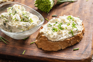 A bowl of homemade cream cheese spread with chopped chives surrounded by bread slices with spread and a bunch of freshly cut chives - obrazy, fototapety, plakaty