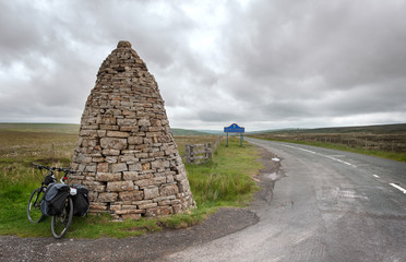 Touring bike leans against a large stone cairn, or currick, at Shorngate Cross on the border of...