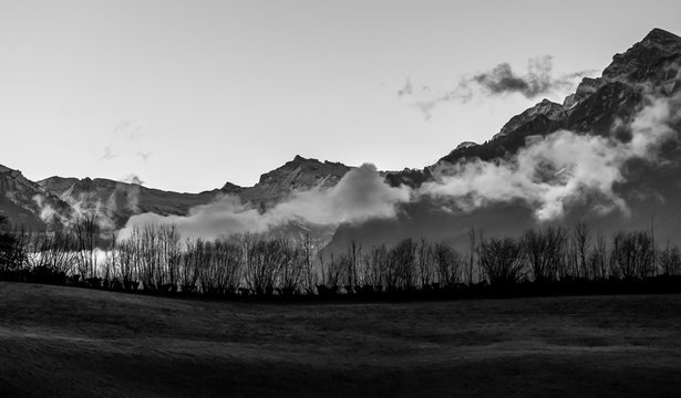 black and white landscape picture of mountains in Switzerland, St. Gallen, in the morning sun with clouds infront of dark silhouettes