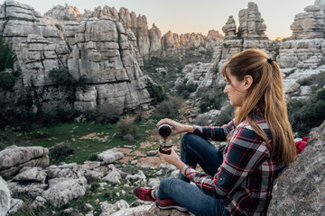 Fototapeta premium Young woman explorer making coffee in a cup on the mountain. Concept of adventure, excursion and trips.