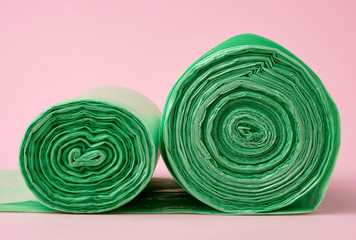 two rolls green plastic bags for trash bin on pink background