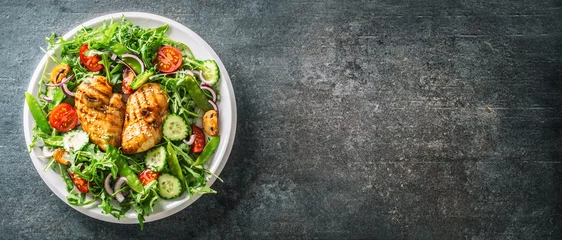 Tuinposter Top view of a healthy chicken salad in a white plate placed on the left half of the black rustic surface © weyo