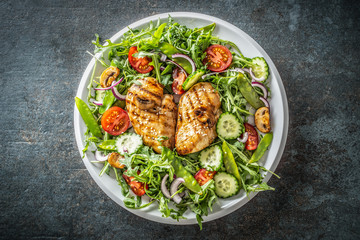 Top view of a healthy chicken salad in a white plate placed on the black rustic surface