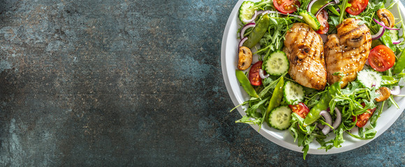 Top view of a healthy chicken salad in a white plate placed on the right half of the black rustic surface