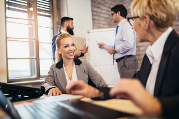 Senior and young colleagues women sitting in modern office using laptop.