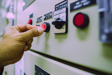 Male engineer wearing a yellow uniform and wearing a white safety hat, inspecting electrical systems in a large power plant