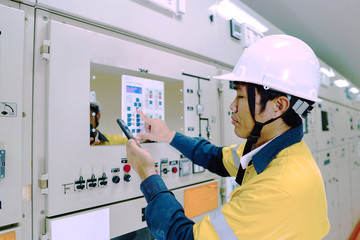 Male engineer wearing a yellow uniform and wearing a white safety hat, inspecting electrical systems in a large power plant