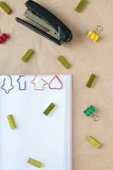 Opened notebook with shaped paper clips on a page, surrounded by binder clips, staples and stapler