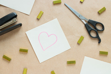 A pair of cissors and a sticky note with a picture of a heart, placed on an opened notebook