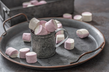 Metallic vintage tray, surface and cup with pink and white marshmallows inside the cup and scattered around the tray as well as in the metallic box in the background