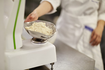 A chef reaching for a weighed bowl of ingredients in a professional restaurant kitchen